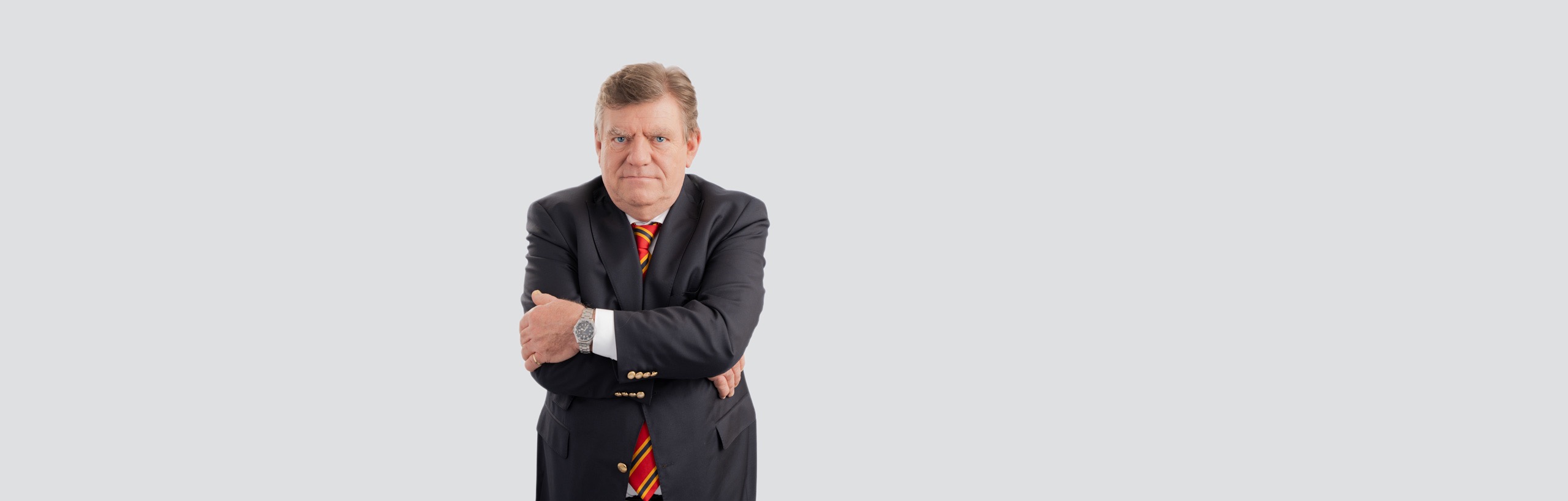 Das Bild zeigt Herrn Uwe Walter im Anzug mit einer gestreiften Krawatte, der mit ernstem Gesichtsausdruck und verschränkten Armen leicht nach links versetzt vor einem sehr hellen, fast weißen Hintergrund steht.